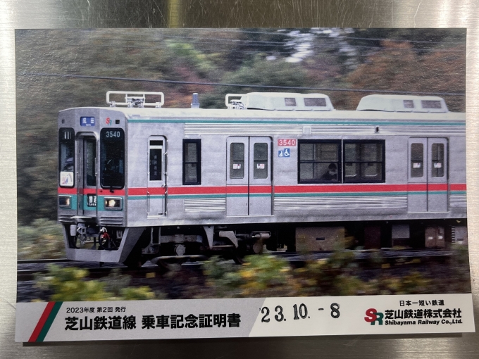 鉄道乗車記録の写真:鉄道グッズ(1)        「芝山千代田駅では、改札口で申告すると「乗車記念証明書」を貰える。
1年に何度かデザインが変わるようなので、コンプしたい人は何度も乗らねばならない。
大きさはハガキサイズ…と言うか、ポストカードそのもの(裏に切手貼付欄や郵便番号欄が印刷されている)」
